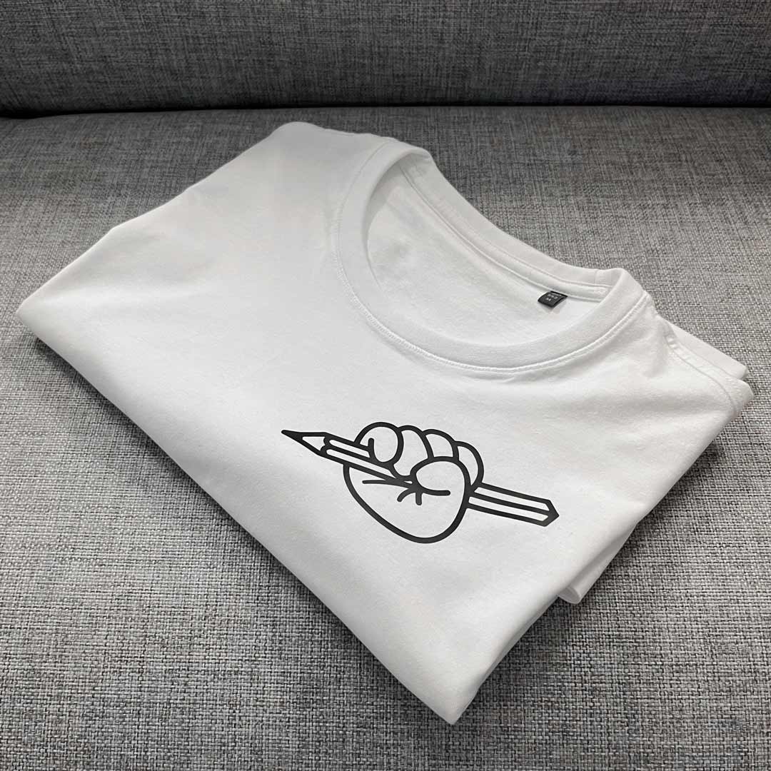White folded T-shirt from Kidler Goods 'Art at Heart' fist holding up a pencil